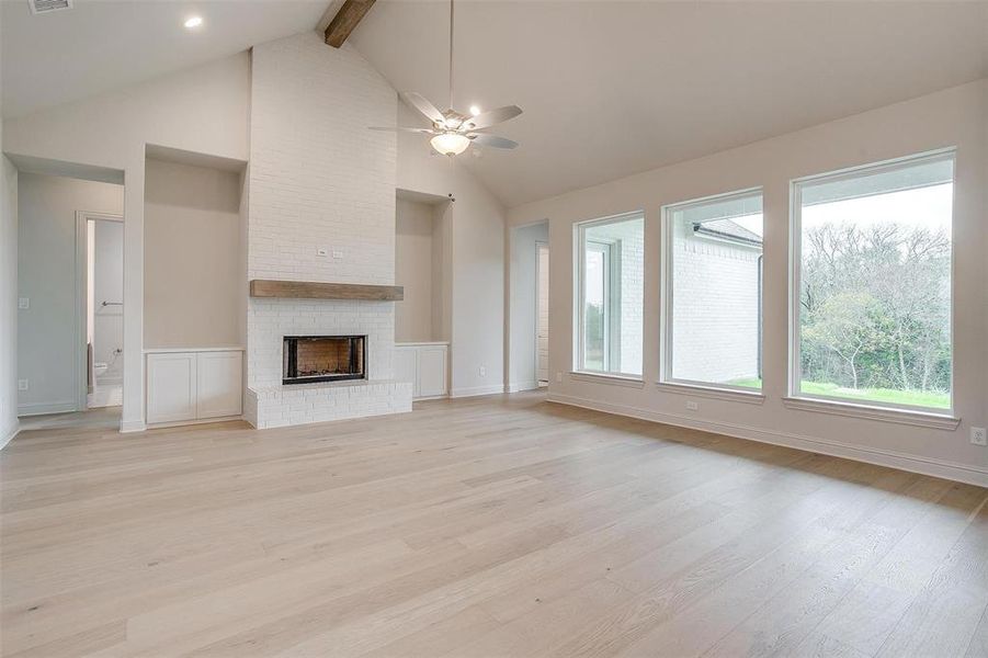 Unfurnished living room with a brick fireplace, high vaulted ceiling, ceiling fan, beam ceiling, and light wood-type flooring