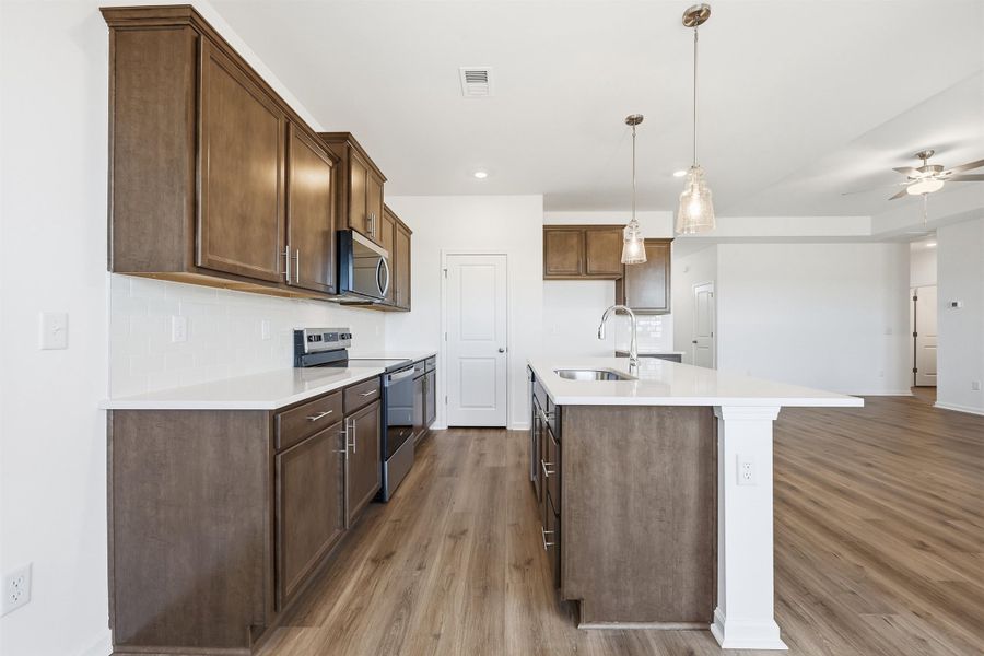 Kitchen with appliances with stainless steel finishes, pendant lighting, an island with sink, a ceiling fan, and light stone counters
