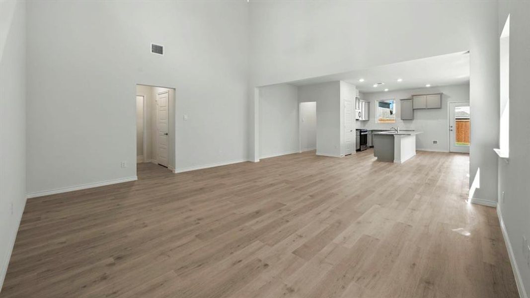 Unfurnished living room featuring a towering ceiling, light wood finished floors, and recessed lighting