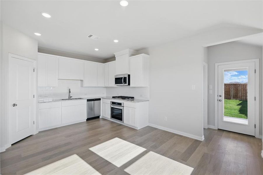 Kitchen featuring appliances with stainless steel finishes, tasteful backsplash, light wood-type flooring, white cabinets, and recessed lighting Kitchen featuring appliances with stainless steel finishes, tasteful backsplash, light wood-type flooring, white cabinets, and recessed lighting