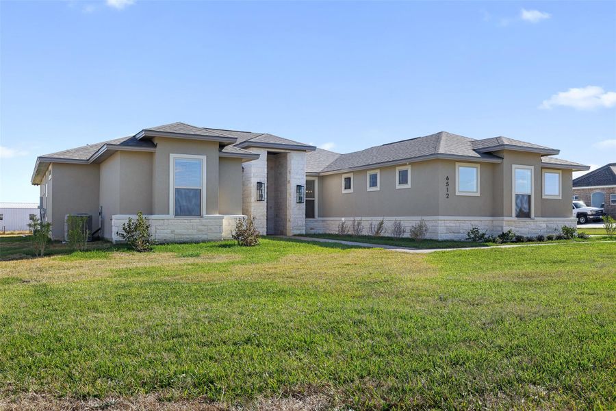 View of front of home featuring a front lawn, stone siding, stucco siding, and a shingled roof