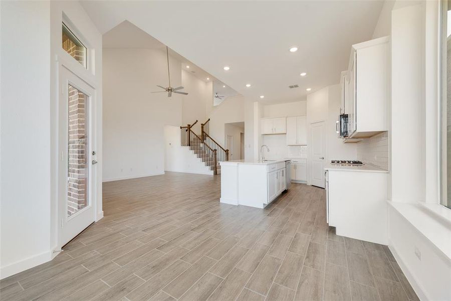 Kitchen with a kitchen island with sink, high vaulted ceiling, white cabinets, sink, and light hardwood / wood-style floors