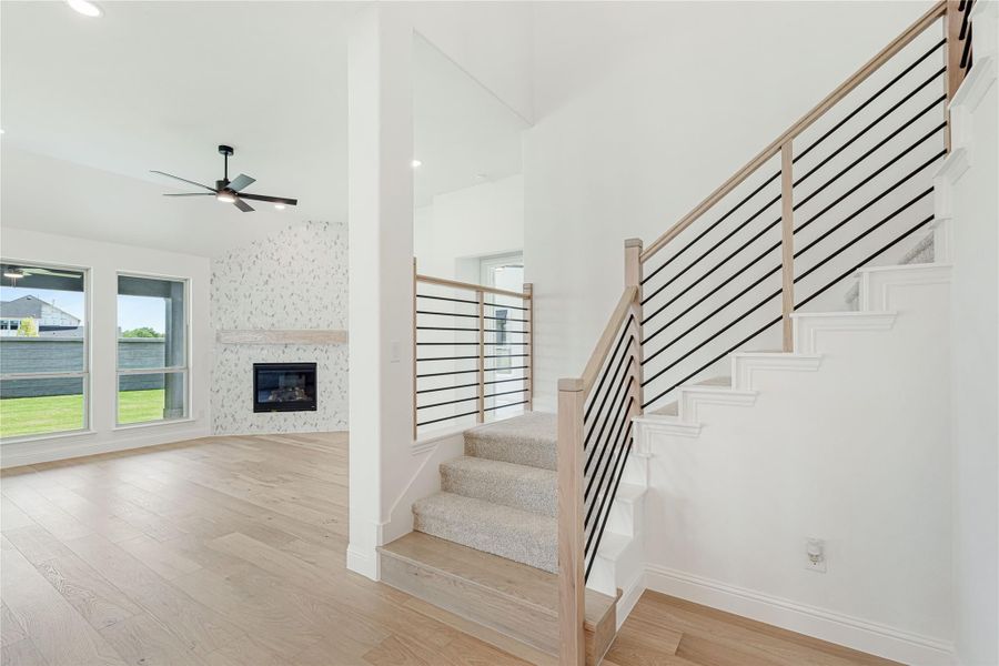 Open living area with staircase featuring wood and black metal railing, fireplace, and hardwood floors Open living area with staircase featuring wood and black metal railing, fireplace, and hardwood floors