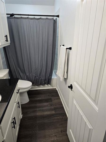 Full bathroom with wood-type flooring, vanity, toilet, and shower / tub combo with curtain