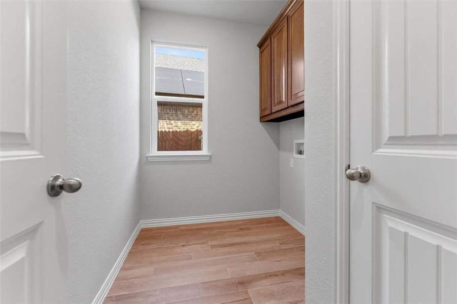 Laundry area with light wood-style floors, hookup for a washing machine, and cabinet space