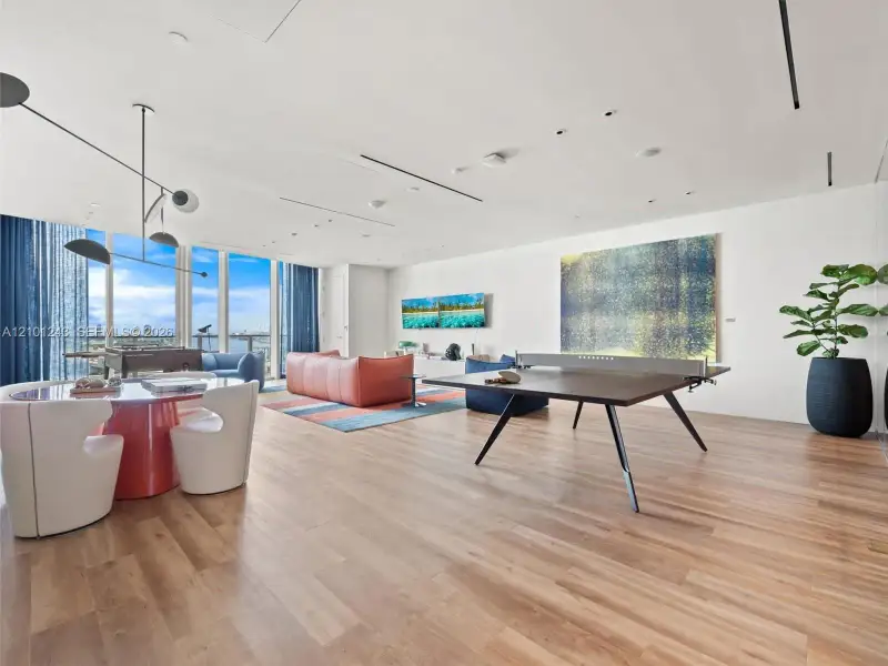 Open-concept interior featuring floor-to-ceiling windows, wood-finish flooring, recessed linear lighting, and modern multi-arm pendant lighting Open-concept interior featuring floor-to-ceiling windows, wood-finish flooring, recessed linear lighting, and modern multi-arm pendant lighting