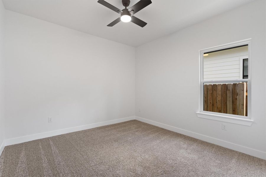 Bright interior room featuring neutral-toned carpet, white walls, and a modern ceiling fan with integrated lighting