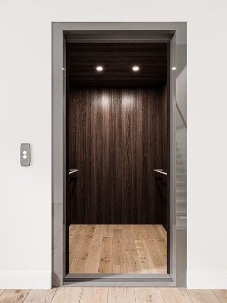 This photo shows a modern home elevator with a sleek design featuring dark wood paneling, recessed lighting, and hardwood flooring, perfect for convenient multi-level access. Virtually Staged.
