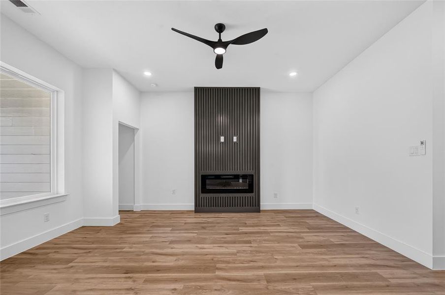 Contemporary interior featuring wood-finish flooring and an accent wall with a built-in electric fireplace Contemporary interior featuring wood-finish flooring and an accent wall with a built-in electric fireplace