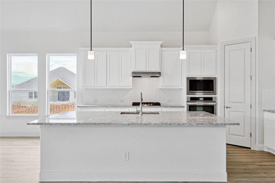 Kitchen with light stone countertops, white cabinetry, an island with sink, light wood-type flooring, and vaulted ceiling