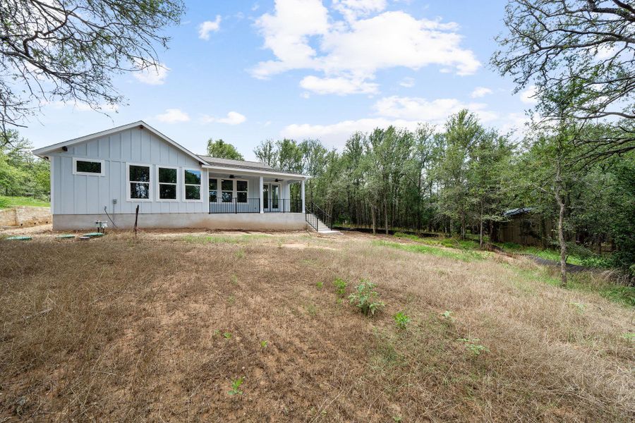 Contemporary light blue board and batten siding, multiple large windows, covered back porch, and mature trees surrounding the property
