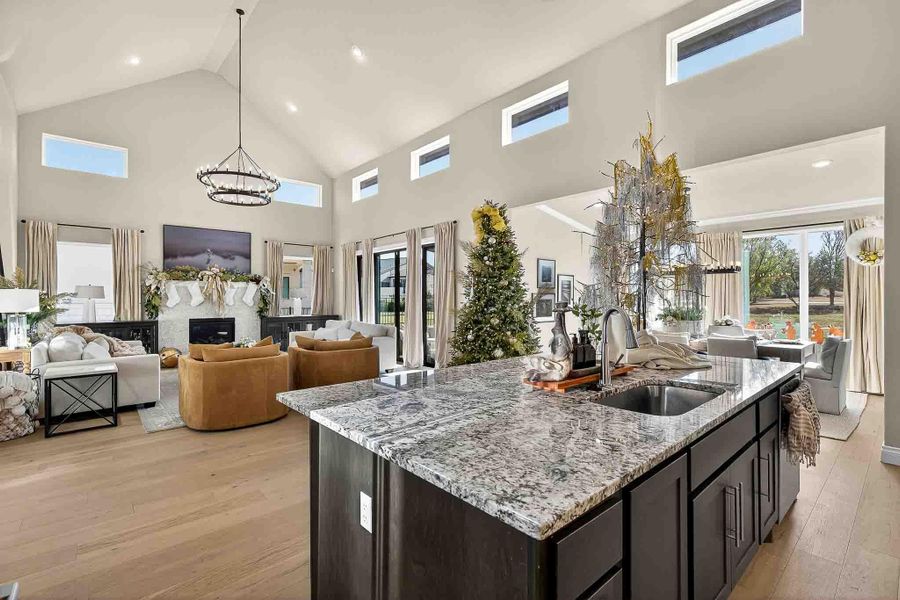 Kitchen featuring open floor plan, high vaulted ceiling, a chandelier, light stone counters, and light wood-style flooring