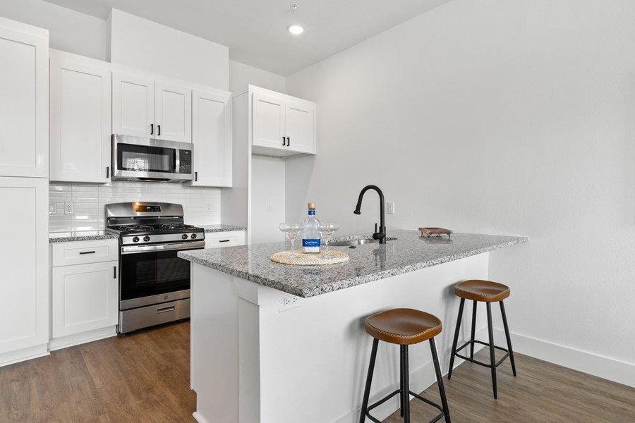 Kitchen featuring a kitchen bar, appliances with stainless steel finishes, white cabinets, decorative backsplash, and light stone counters