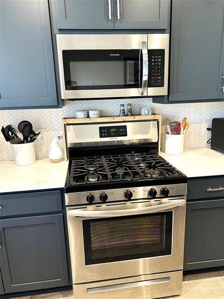 A closeup of the gas range and microwave with pretty herringbone backsplash