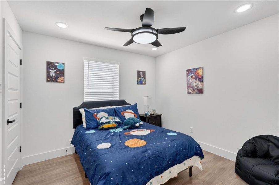 Bedroom featuring a black ceiling fan with integrated lighting, recessed ceiling lights, and wood-finish flooring