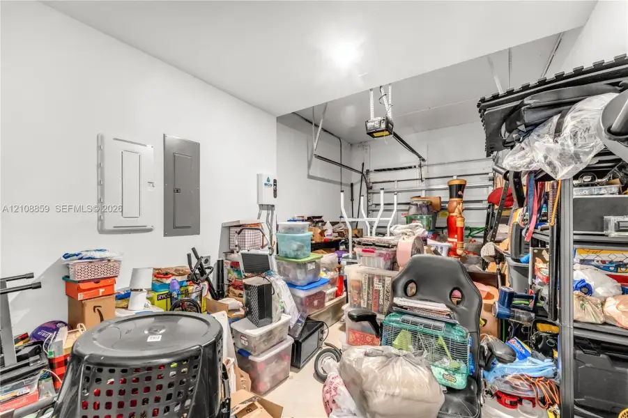 Enclosed garage space featuring an overhead automatic door opener, dual electrical service panels, and a tankless water heater