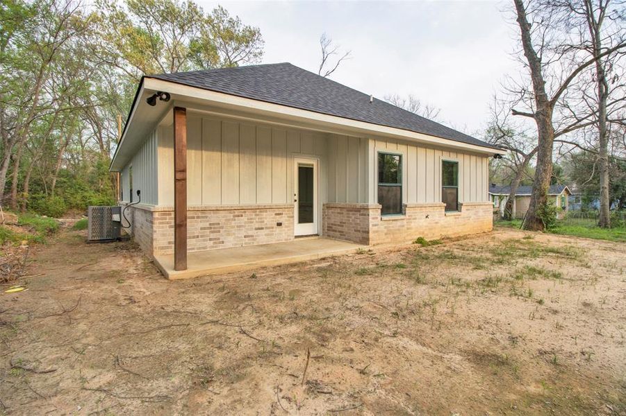 Back of property featuring board and batten siding, a shingled roof, and brick siding
