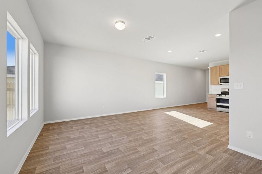 Image of a living room with light grey walls, brown wood-look vinyl flooring, and two windows