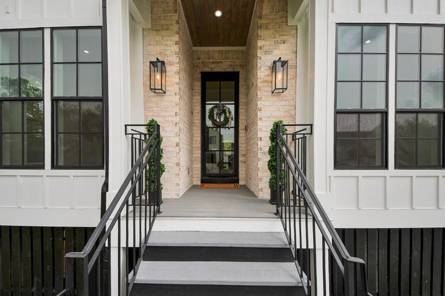Welcome guests into this inviting home through a charming, covered entryway featuring elegant lantern lighting, stylish wrought-iron railings, and an impressive glass-paneled front door, setting the tone for the warm and welcoming ambiance found throughout this beautiful Timbergrove Manor property.