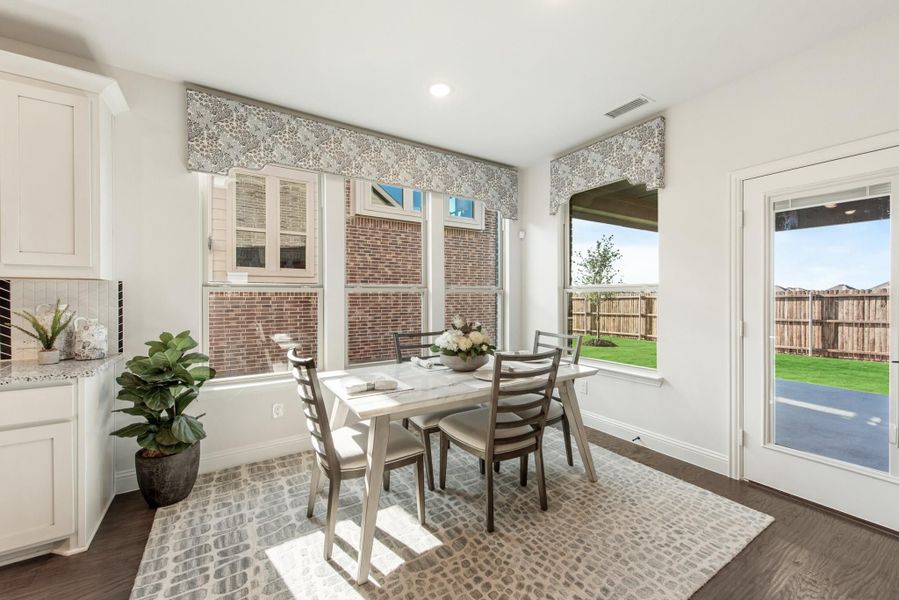 Breakfast nook with white dining table, four chairs, hardwood floors, and large windows overlooking a fenced backyard