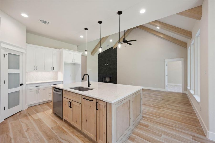 Kitchen with sink, lofted ceiling with beams, white cabinetry, and an island with sink