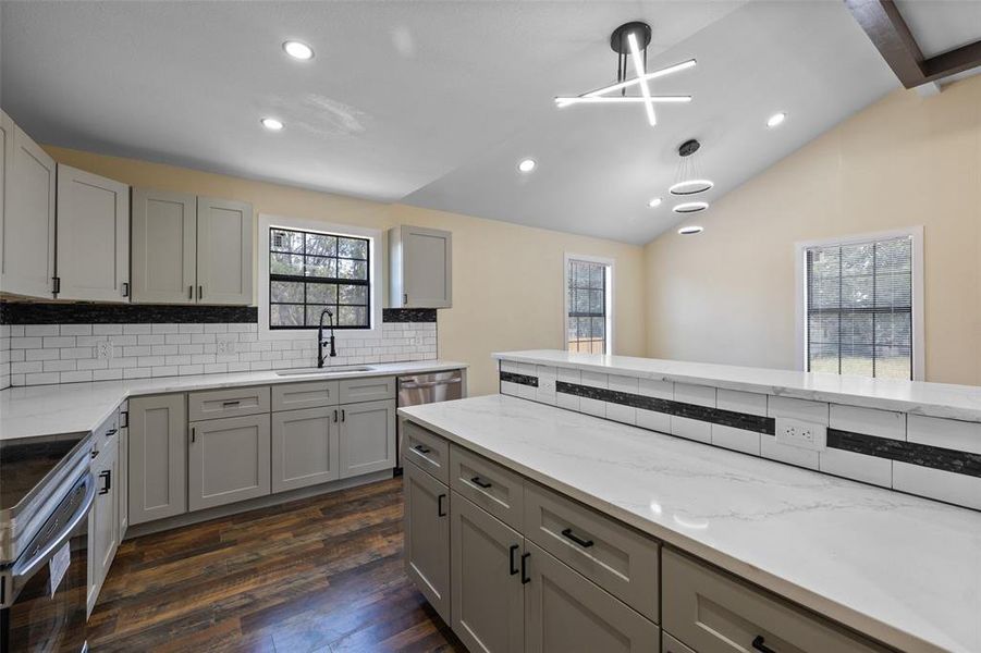 Kitchen with decorative light fixtures, sink, lofted ceiling with beams, backsplash, and dark wood-type flooring