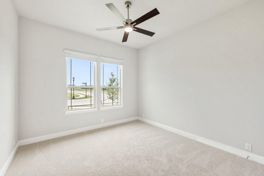 Empty bedroom with ceiling fan, carpet flooring, and double windows overlooking a neighborhood street
