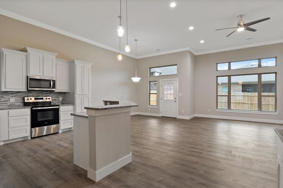 Kitchen featuring white cabinets, dark wood-type flooring, a kitchen island, appliances with stainless steel finishes, and decorative backsplash