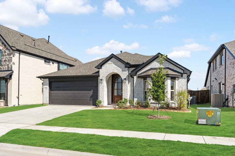 Single-story home with white brick exterior, arched entry, two-car dark garage, and green front lawn