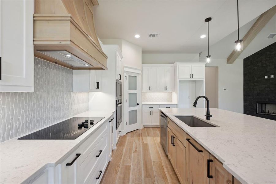 Kitchen with sink, hanging light fixtures, light stone countertops, custom range hood, and white cabinetry