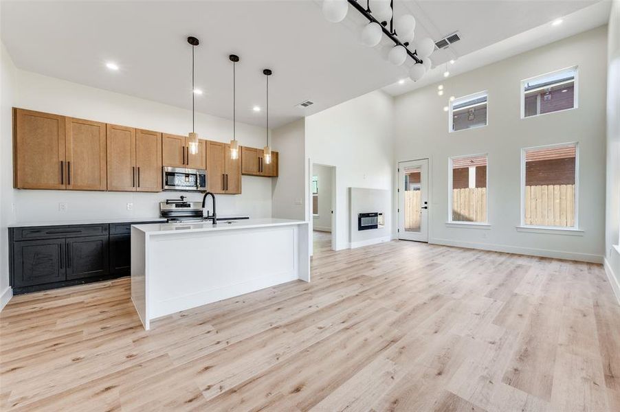 Kitchen with a center island with sink, hanging light fixtures, a high ceiling, stainless steel appliances, and light wood-type flooring