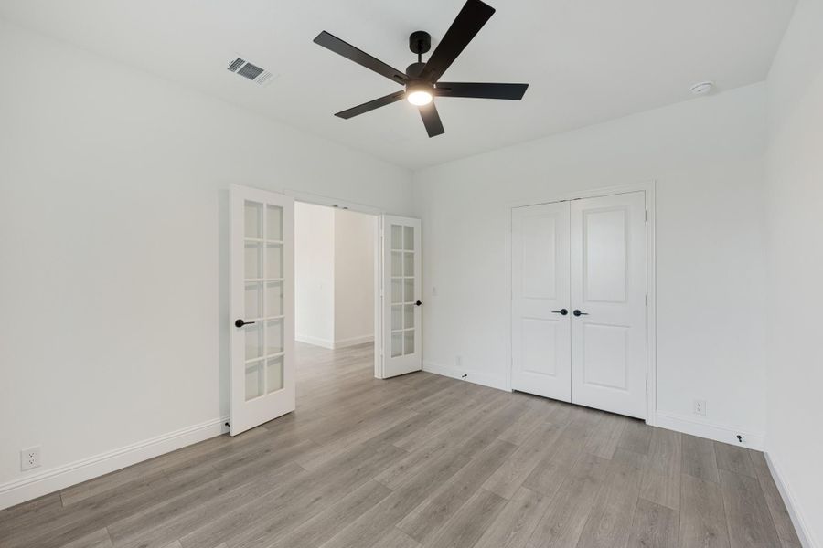 Empty bedroom with gray wood floors, black ceiling fan, French doors, and a double closet