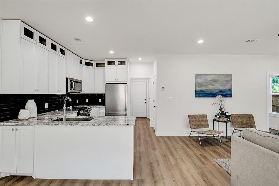 Kitchen featuring sink, wood-style flooring, white cabinetry, appliances with stainless steel finishes, and light granite countertops