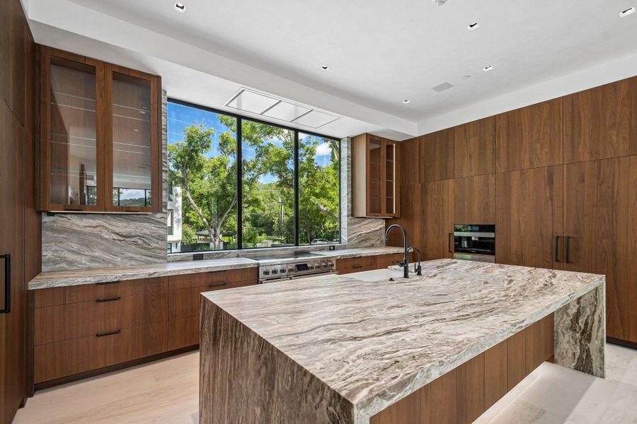 Rich wood cabinetry surrounds a waterfall stone island beneath soaring ceilings and expansive windows. Rich wood cabinetry surrounds a waterfall stone island beneath soaring ceilings and expansive windows.