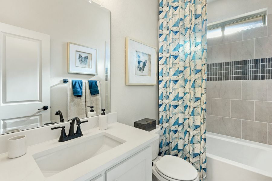 Bathroom with white vanity, black faucet, and tub-shower combo with gray tile and blue patterned curtain Bathroom with white vanity, black faucet, and tub-shower combo with gray tile and blue patterned curtain