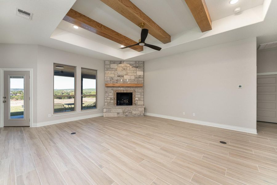 Unfurnished living room with wood finish floors, recessed lighting, beamed ceiling, ceiling fan, and a stone fireplace Unfurnished living room with wood finish floors, recessed lighting, beamed ceiling, ceiling fan, and a stone fireplace