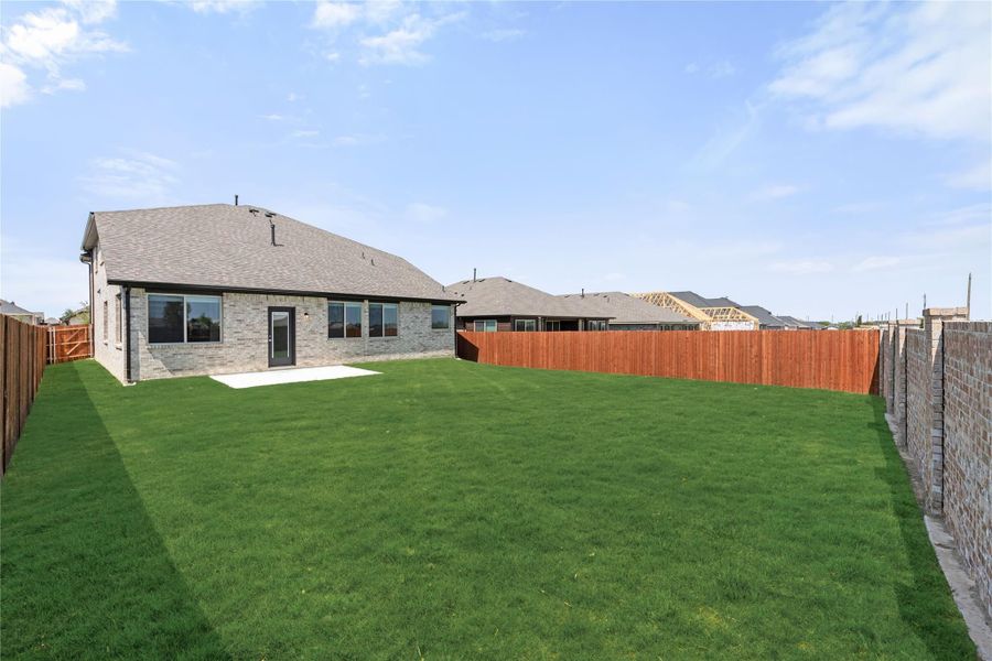 Backyard of brick home with large green lawn, concrete patio, and wood privacy fence