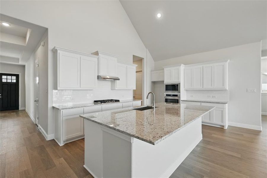 Kitchen featuring backsplash, white cabinets, a kitchen island with sink, dark wood finished floors, and a high ceiling
