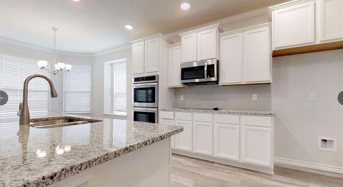 Kitchen with appliances with stainless steel finishes, a sink, backsplash, white cabinetry, and light wood-style floors