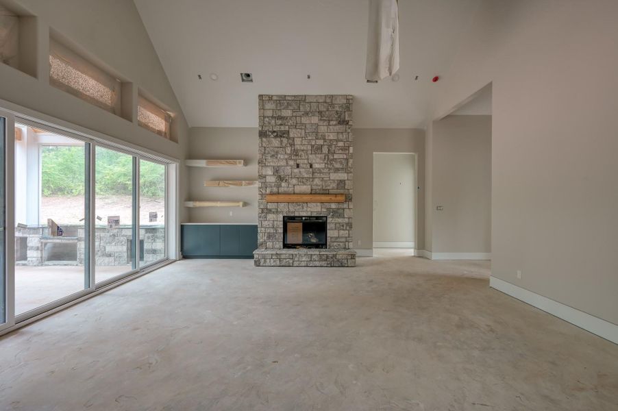 This spacious living room features high ceilings, a large stone fireplace, and ample natural light from expansive windows. The neutral color palette and open layout offer a versatile space.
