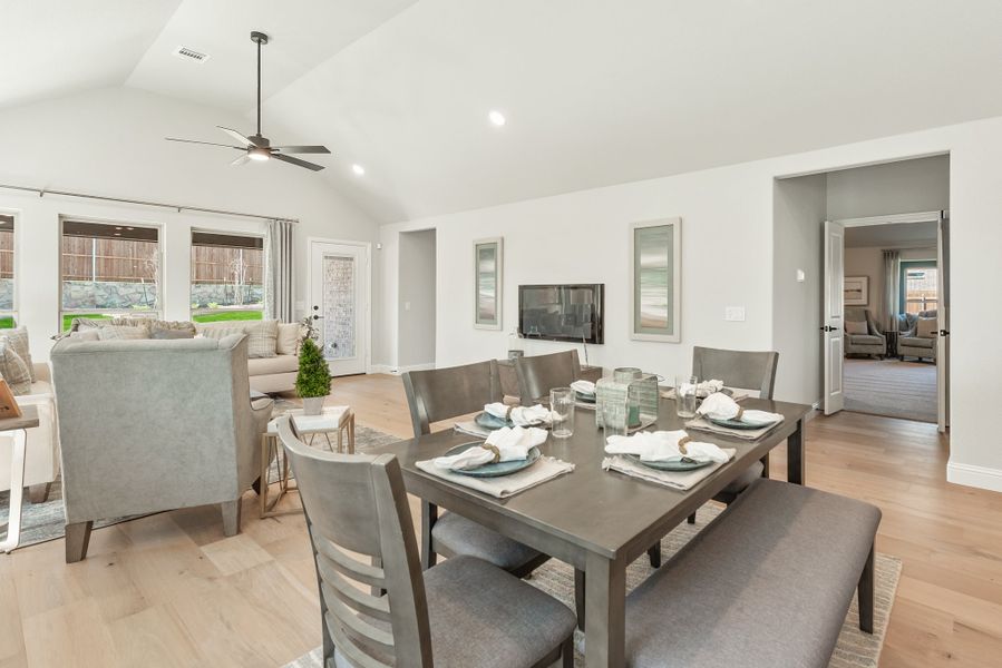 Open-concept dining and living area with vaulted ceiling, ceiling fan, wood floors, and set dining table with bench seating.