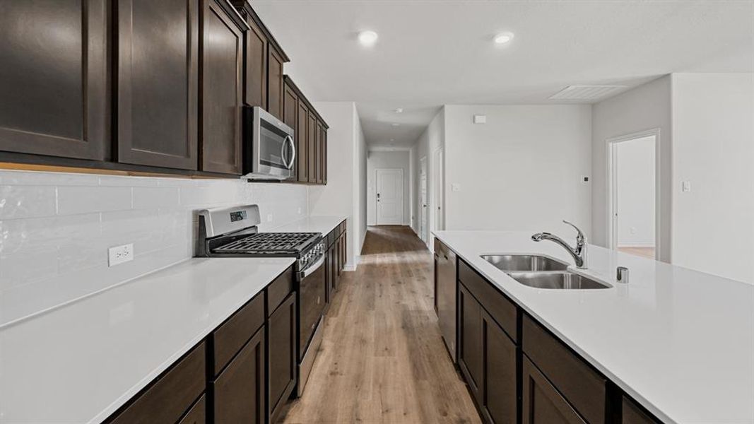 Galley kitchen featuring dark wood-finish cabinetry, white solid surface countertops, a white subway tile backsplash, stainless steel appliances, and wood-finish flooring