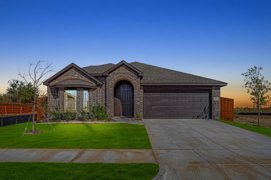 Single-story brick home with arched entry, two-car garage, and green front lawn at dusk