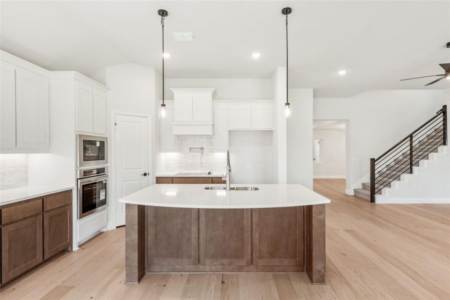 Kitchen with large center island, white upper cabinets, stainless steel ovens, pendant lights, and light hardwood floors