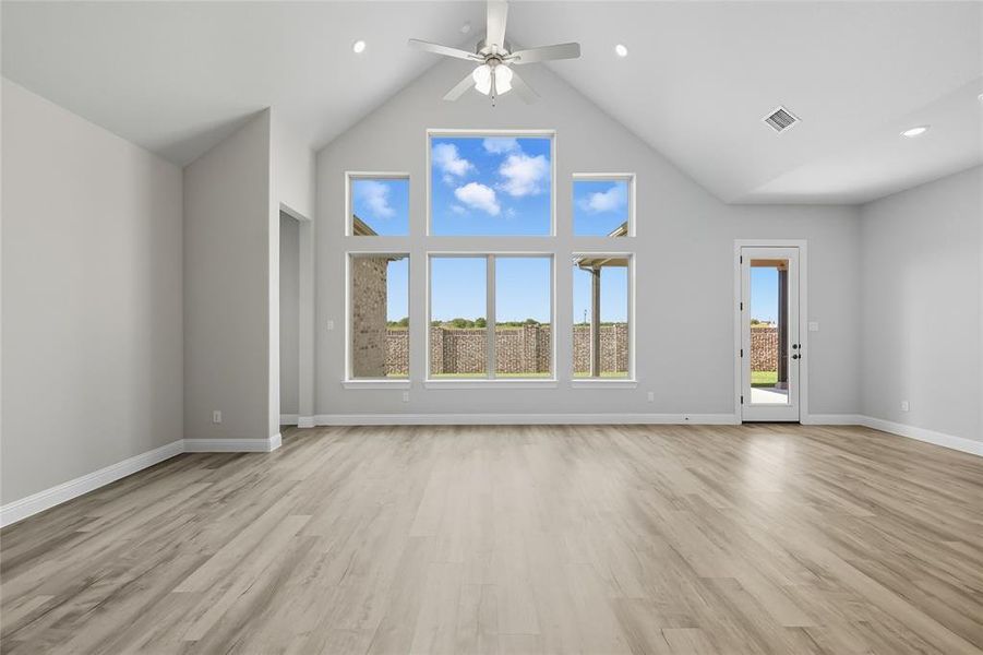Unfurnished living room featuring ceiling fan, light wood-style floors, a high ceiling, and plenty of natural light