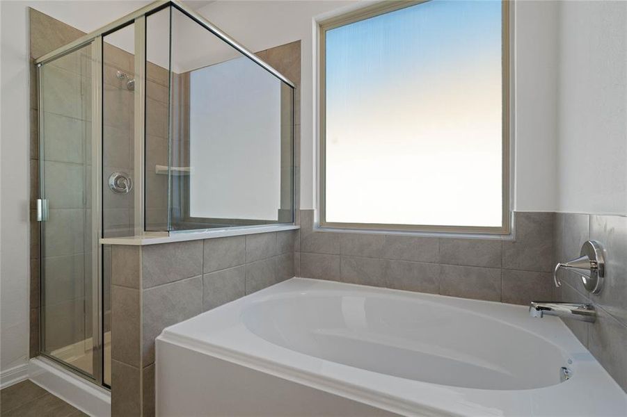 The additional view of the primary bathroom displays the separate garden tub, large window and walk-in shower with tile surround.