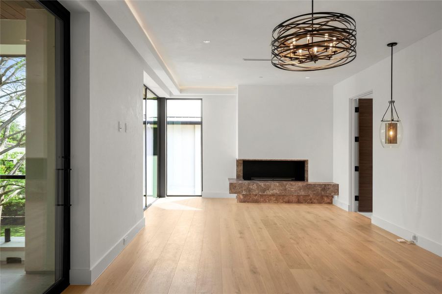 Primary bedroom featuring light wood-style flooring, hanging lights, and a fireplace with raised hearth