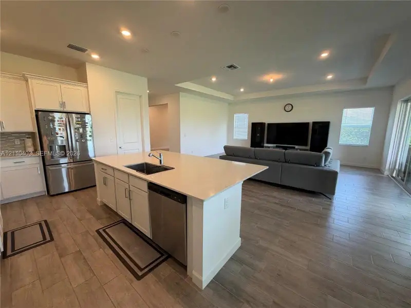 Kitchen island featuring a stone countertop, undermount stainless steel sink, and built-in stainless steel dishwasher, complemented by recessed ceiling lighting and wood-finish tile flooring