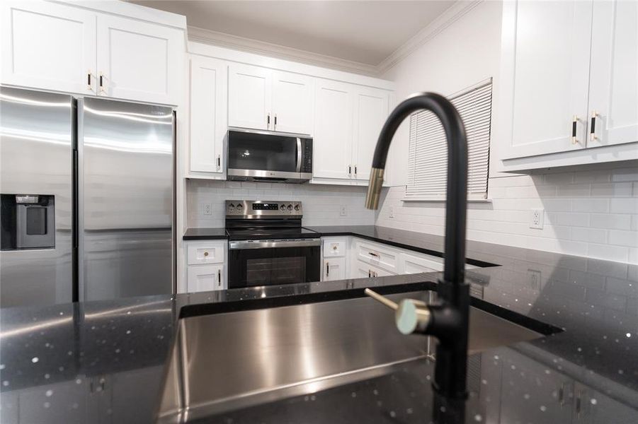 Kitchen with appliances with stainless steel finishes, dark countertops, crown molding, and backsplash Kitchen with appliances with stainless steel finishes, dark countertops, crown molding, and backsplash