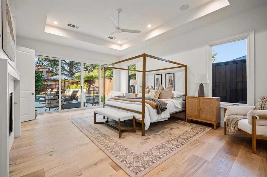 Bedroom featuring multiple windows, a raised ceiling, light hardwood / wood-style floors, and ceiling fan